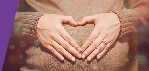 Person putting their hands on their pregnant stomach to form a heart shape.