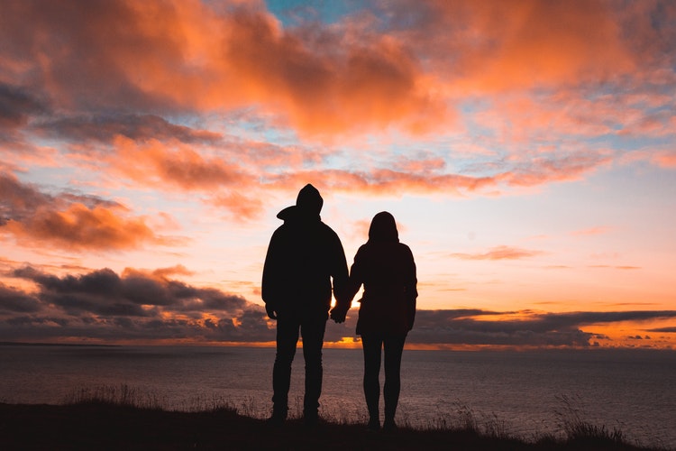 A couple looking at a sunset and holding hands.